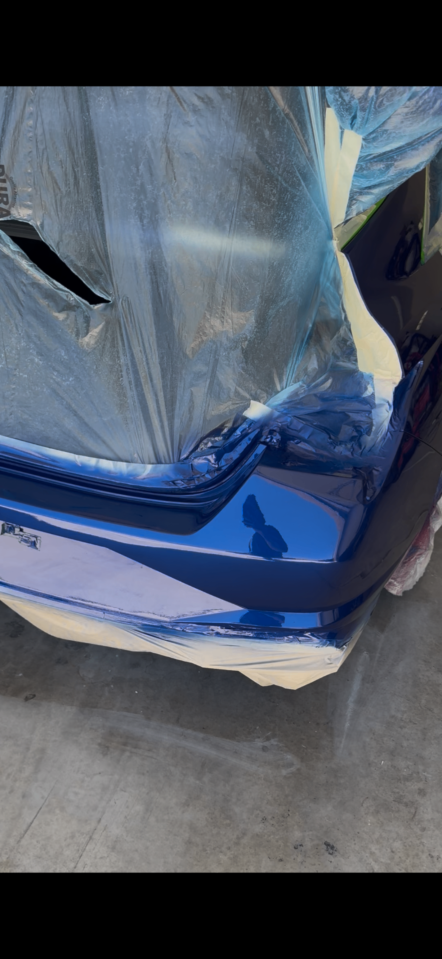 Blue sedan rear bumper masked off mid-respray with fresh paint applied