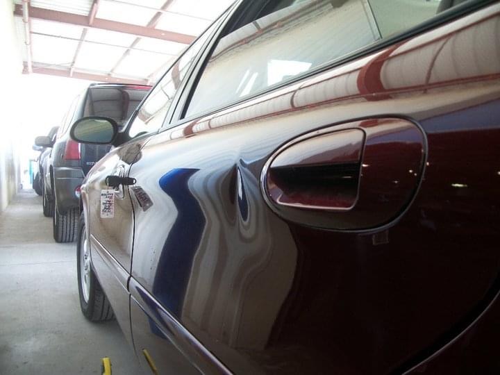 Maroon sedan rear door with dent before paintless dent repair